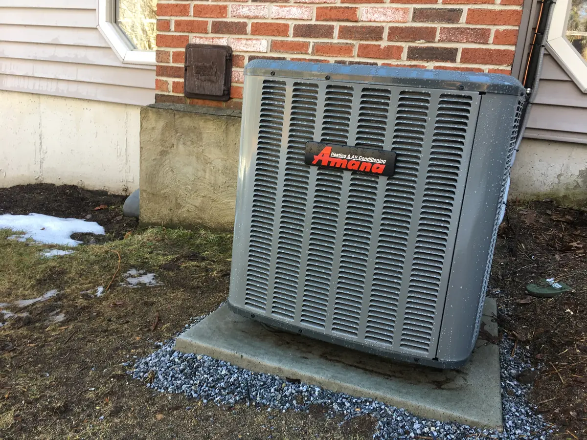 Amana central air conditioner condenser installed beside a brick and clapboard Southern NH home by A.J. LeBlanc Heating