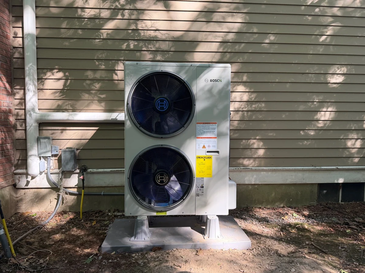 Bosch dual-fan heat pump installed on a raised base beside a home