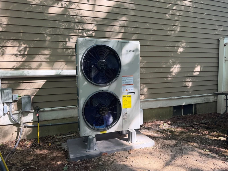 Bosch dual-fan heat pump installed on a raised base beside a home