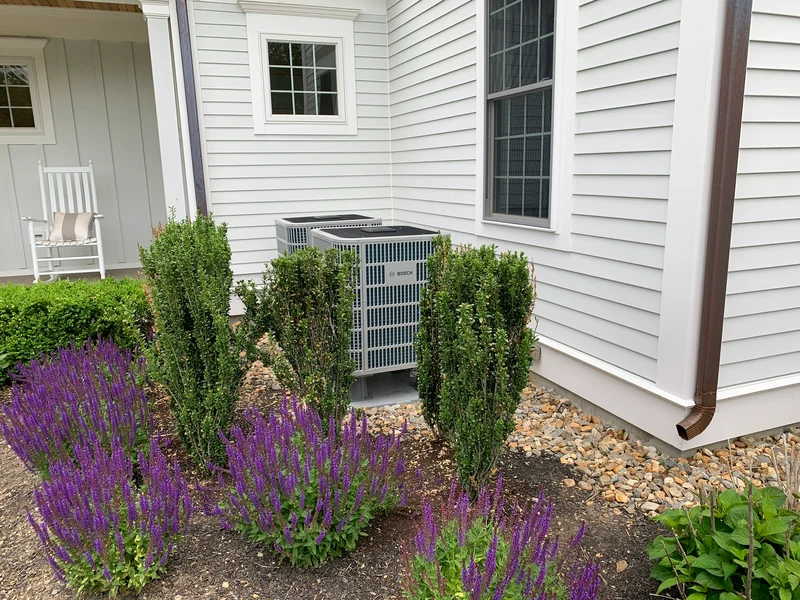 Pair of Bosch outdoor heat pump units with mature landscaping at a Southern NH home