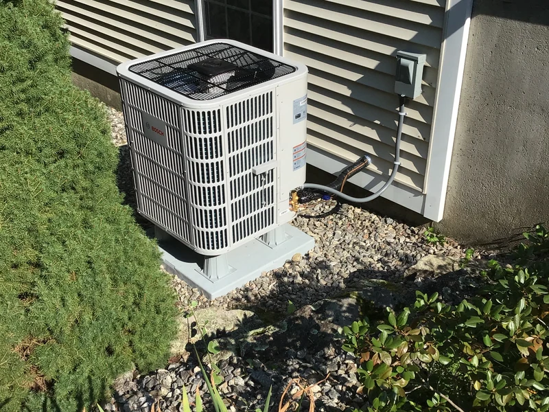 Bosch outdoor unit on a raised base beside a gray-sided home