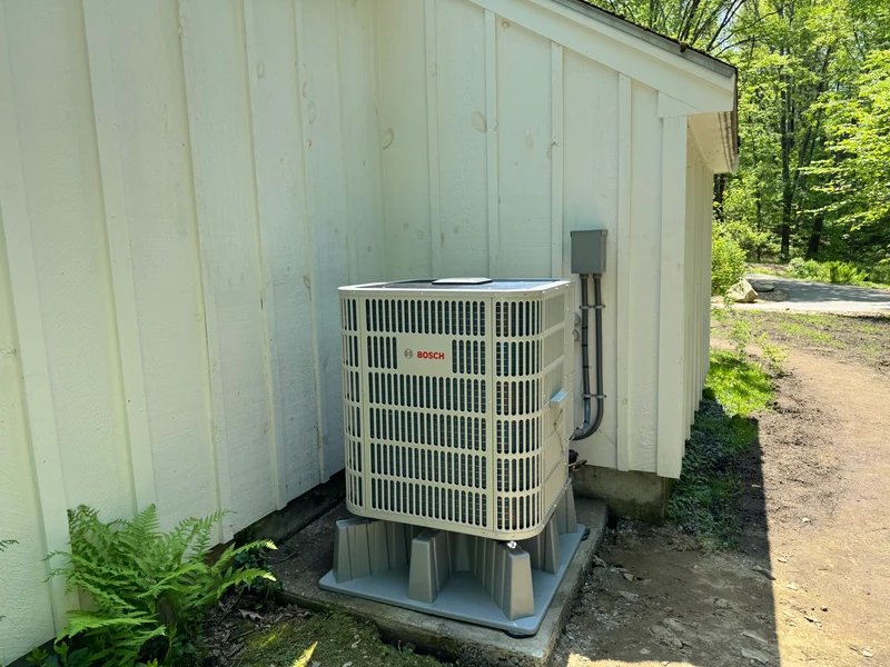 Bosch outdoor unit on a raised base beside white siding