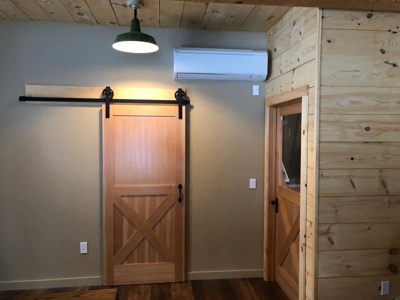 Ductless mini split indoor head installed above a sliding barn door in a rustic Southern NH interior