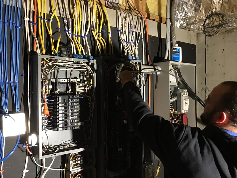 A.J. LeBlanc Heating licensed electrician wiring a 200-amp main panel, generator transfer switch, and sub-panel in a Southern NH home