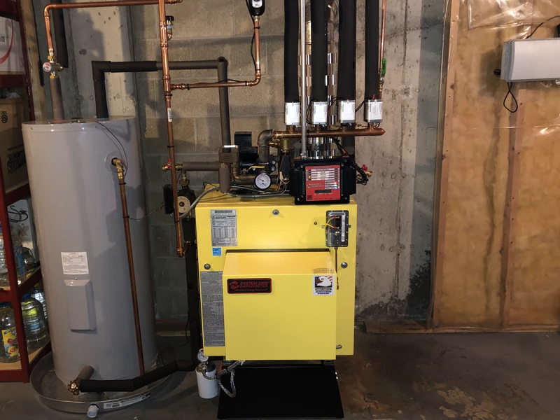 Energy Kinetics System 2000 oil boiler with multi-zone copper manifold next to a tank water heater in a Southern NH basement