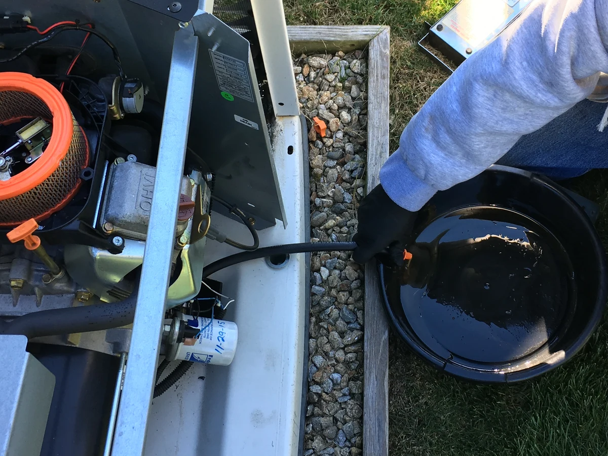 A.J. LeBlanc Heating technician performing an annual oil change on a residential standby generator in Southern NH, with the drain pan and air filter visible