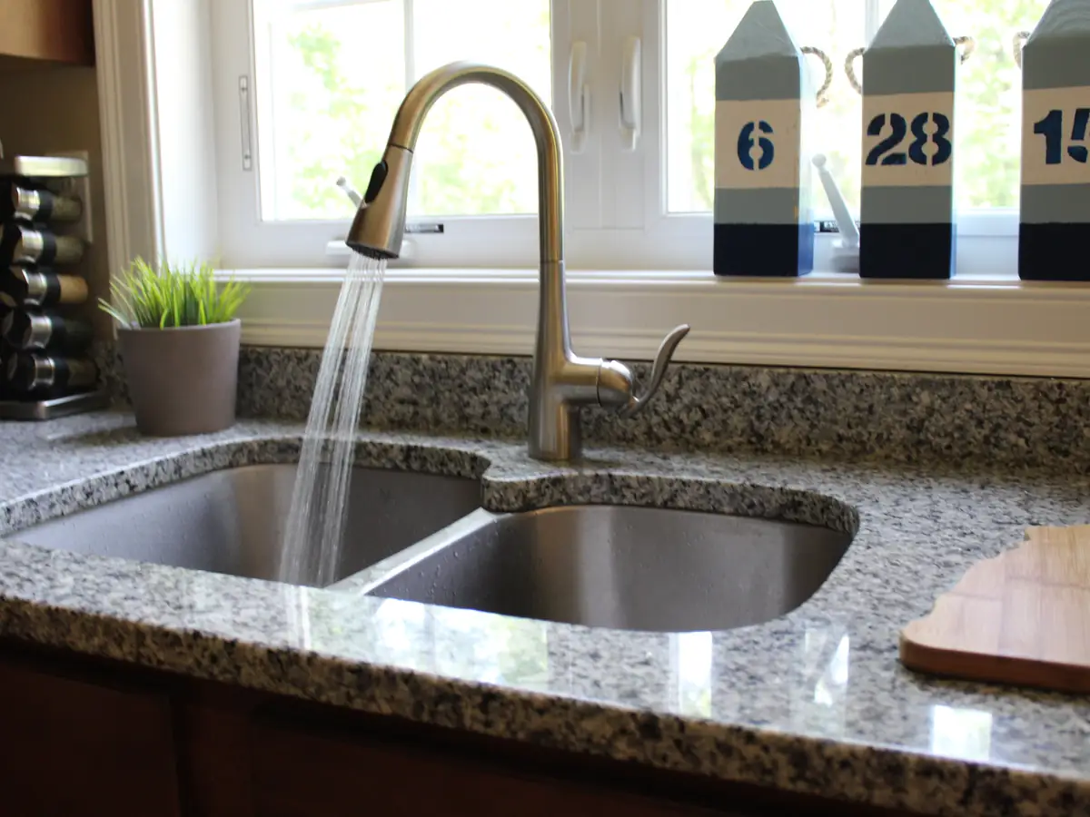 New kitchen faucet installation over a granite countertop with double-bowl sink by A.J. LeBlanc Heating licensed plumbers in a Southern NH home