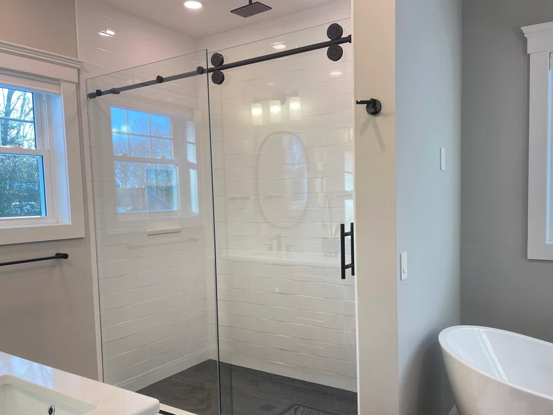 Large subway tile shower with frameless glass barn door installed by A.J. LeBlanc Heating in a Southern NH home