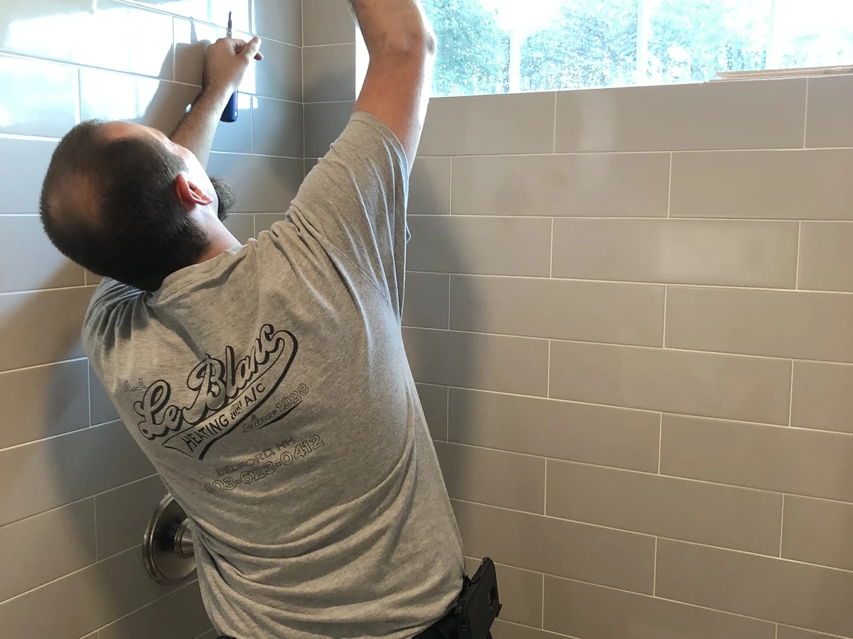 A.J. LeBlanc Heating plumber installing a shower head in a new gray subway tile shower in a Southern NH home