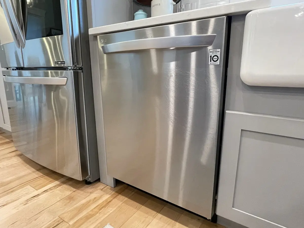 LG stainless steel dishwasher hooked up between a French-door refrigerator and farmhouse sink by A.J. LeBlanc Heating in a Southern NH kitchen