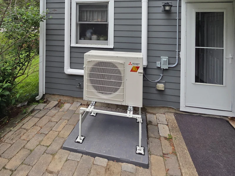 Mitsubishi outdoor mini-split unit on a raised stand beside a gray-sided home