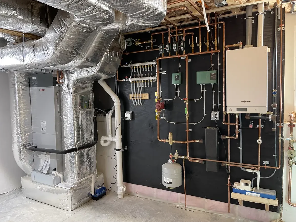 A.J. LeBlanc Heating mechanical room install with an air handler, insulated ductwork, and a wall-hung condensing boiler with a multi-zone hydronic manifold in a Southern NH home