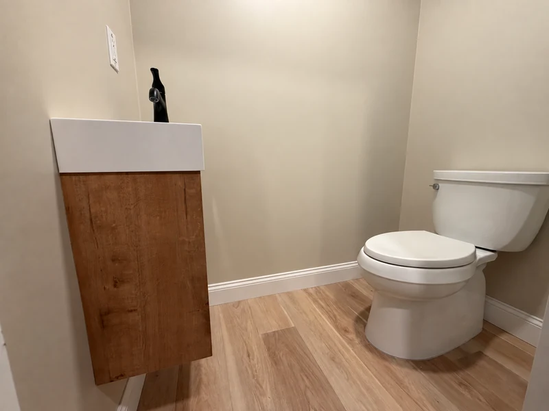 Powder room with a white toilet beside a floating wood vanity and white sink