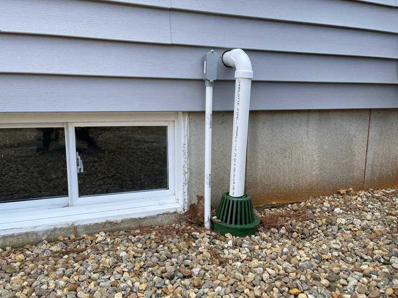 Exterior sump-pump discharge piping carrying water away from the foundation, installed by A.J. LeBlanc Heating in Southern NH