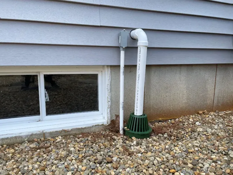Exterior sump-pump discharge piping carrying water away from the foundation, installed by A.J. LeBlanc Heating in Southern NH
