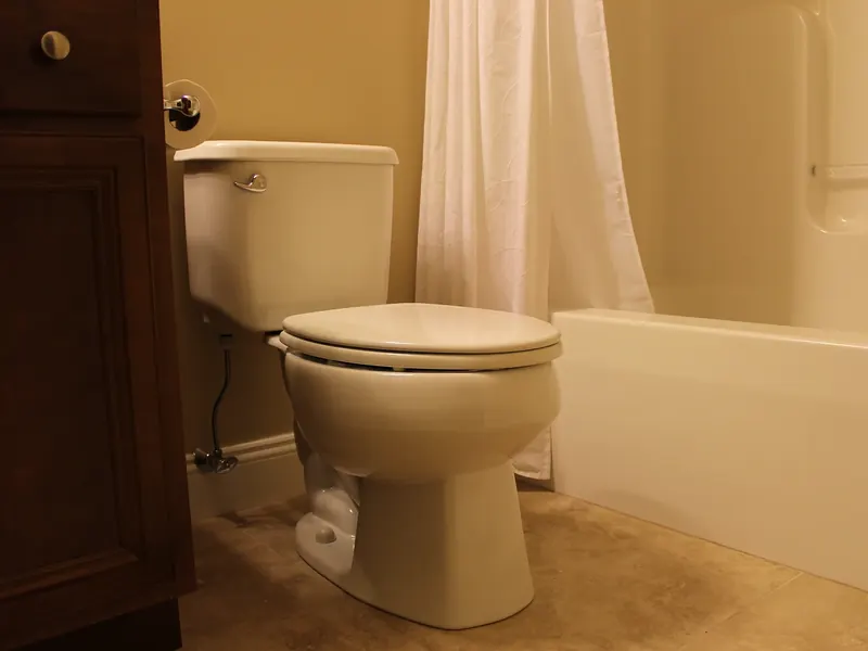 White two-piece toilet installed by A.J. LeBlanc Heating beside a vanity and tub-shower combination in a Southern NH bathroom